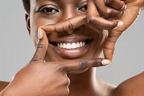 black lady smiling, using her fingers to frame her white teeth